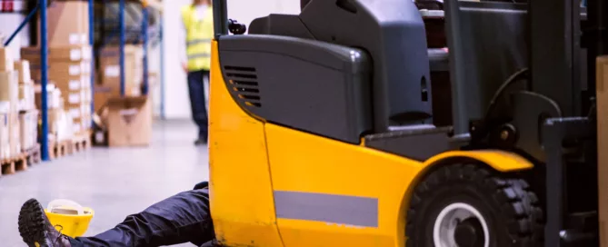 Worker trapped under a forklift in a warehouse accident with a hard hat on the ground, representing a serious workplace injury and potential third-party liability claim beyond workers’ compensation in Wheeling.