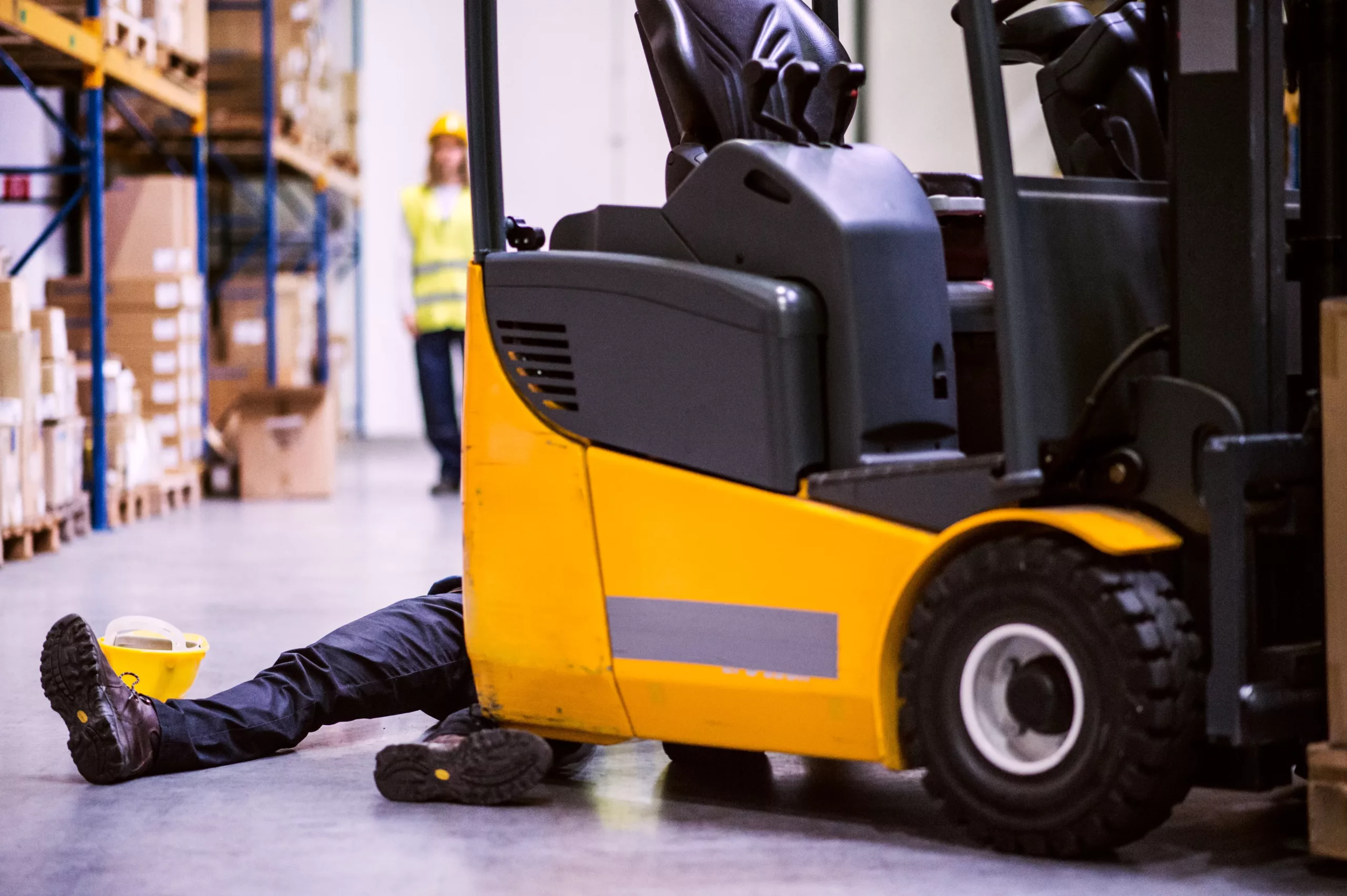 Worker trapped under a forklift in a warehouse accident with a hard hat on the ground, representing a serious workplace injury and potential third-party liability claim beyond workers’ compensation in Wheeling.